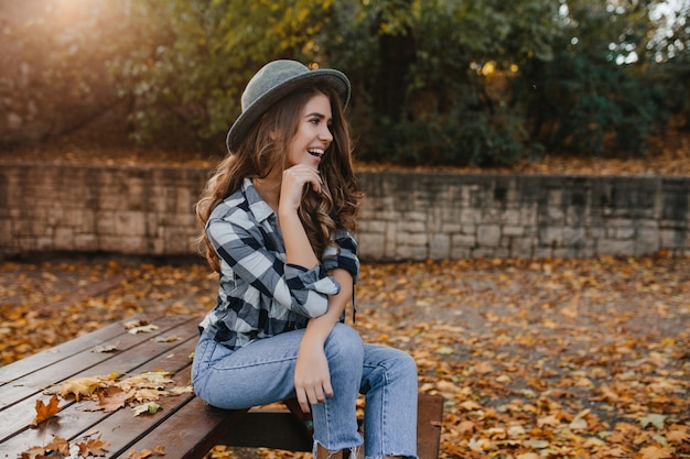 Romantische weiße Frau mit langen braunen Haaren, die mit verträumtem Lächeln wegschauen und im sonnigen Herbsttag aufwerfen