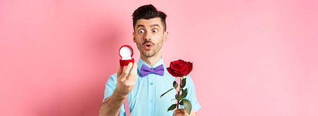 Romantischer lustiger Kerl des Valentinstags, der Hochzeitsantrag machen wird und ihn bitten wird, ihn zu heiraten, der rote Ros hält