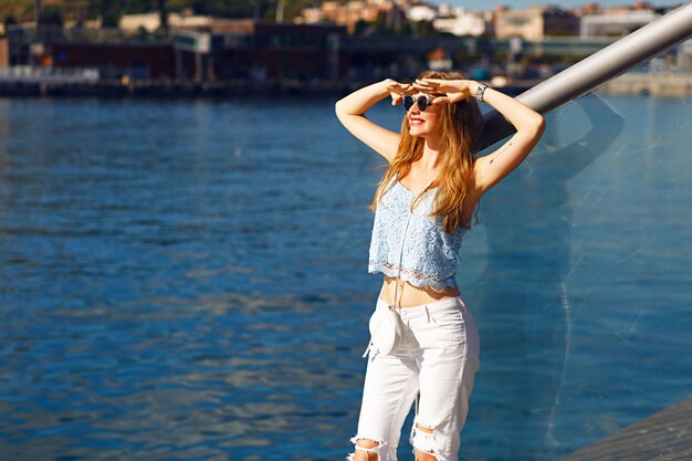 Romantisches Meerblickporträt der sinnlichen blonden Frau, trendiges Sommeroutfit, Pastellfarben, Reisen allein, Urlaub, weißer Denim, Sonnenbrille.