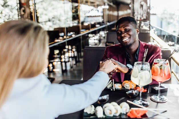 Romantisches Paar im Café trinkt Mojito mit Sushi und genießt das Zusammensein. Mann hält Hand seiner Frau.