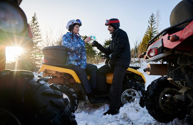 Romantisches Paar im Winter im Freien, das mit blauem Champagner auf gelbem ATV feiert