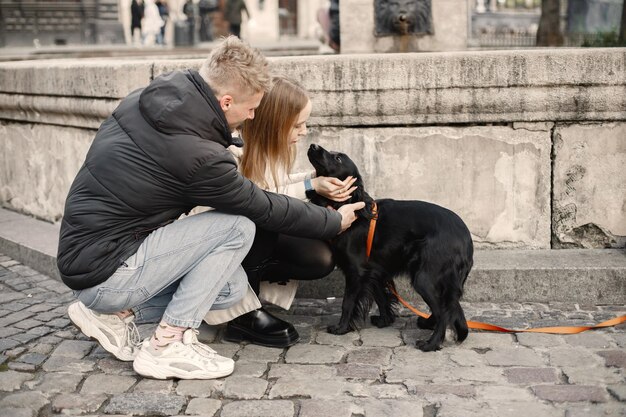 Romantisches Paar steht auf der Straße im Herbst Mann und Frau streicheln einen schwarzen Hund auf einer Straße in der Altstadt Mädchen mit beigem Mantel und schwarzer Jacke des Mannes