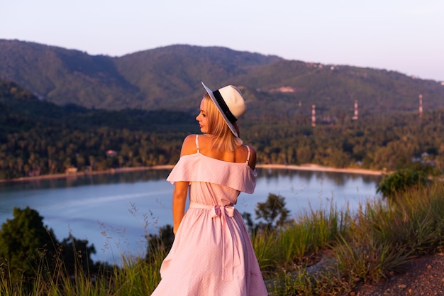 Romantisches Porträt der jungen kaukasischen Frau im Sommerkleid, das das Entspannen im Park auf Berg mit erstaunlichem tropischem Meerblick genießt Frau auf Urlaubsreise durch Thailand Glückliche Frau bei Sonnenuntergang