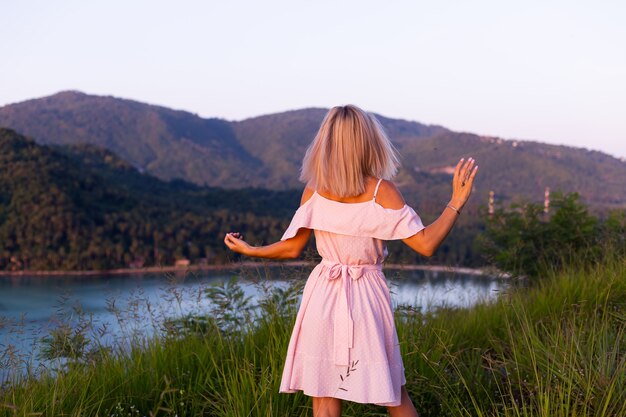 Romantisches Porträt der jungen kaukasischen Frau im Sommerkleid, das das Entspannen im Park auf Berg mit erstaunlichem tropischem Meerblick genießt Frau auf Urlaubsreise durch Thailand Glückliche Frau bei Sonnenuntergang