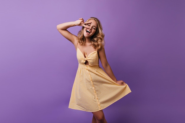 Romantisches schlankes Mädchen mit fröhlichem Gesichtsausdruck, das mit gelbem Kleid spielt Begeisterte kaukasische Dame mit blonden Haaren tanzt im Studio
