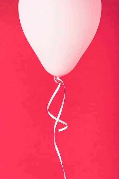 Kostenloses Foto rosa ballon mit band auf rotem hintergrund