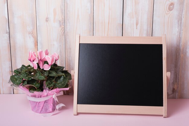 Rosa Blumenblumenstrauß mit kleiner leerer Tafel auf Schreibtisch gegen hölzerne Wand