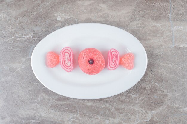 Rosa Geleebonbons und ein Keks, ausgerichtet auf einer Platte auf Marmoroberfläche