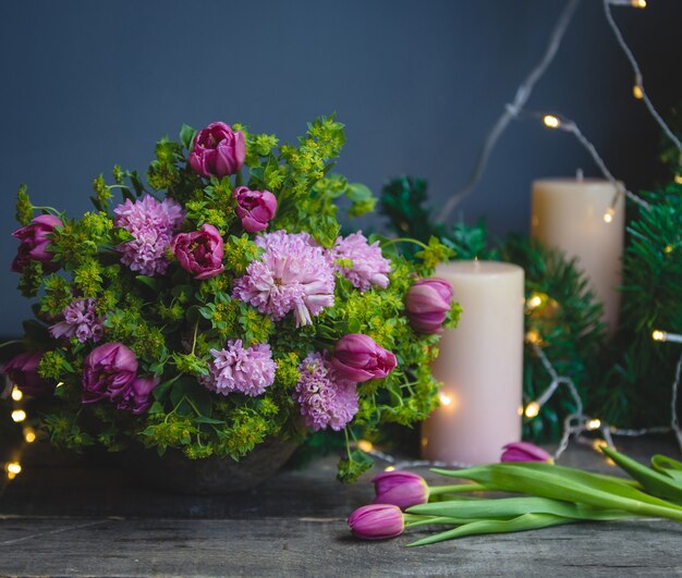 Rosa grüner Blumenstrauß, Tulpen und Kerzen mit Weihnachtslichtern herum