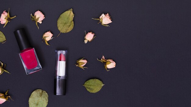 Rosa Lippenstift- und Nagellackflasche mit den rosafarbenen trockenen rosafarbenen Knospen und den Blättern auf schwarzem Hintergrund