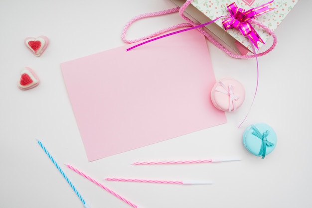Rosa Papier; Macarons; Kerzen und Herz gestalten Süßigkeiten und Einkaufstasche auf weißem Hintergrund