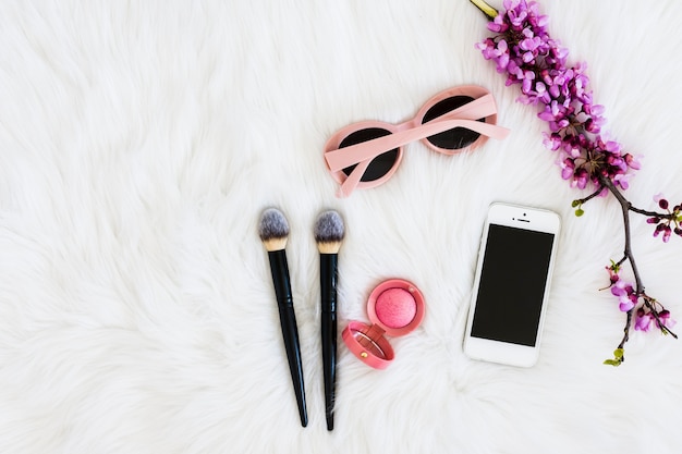 Rosa Sonnenbrillen; lila Blumenzweig; kompaktes Gesichtspuder; Make-up-Pinsel und Handy auf Pelzhintergrund