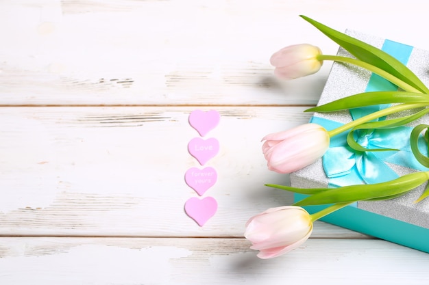 Rosa tulpen mit geschenkbox auf weißem hintergrund aus holz. valentinstag romantischer hintergrund.