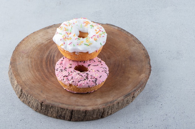 Rosa und weiße Donuts verziert mit Streuseln auf Holzstück