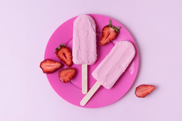 Rosafarbene Eiscreme auf Stöcken und Scheiben der Erdbeeren