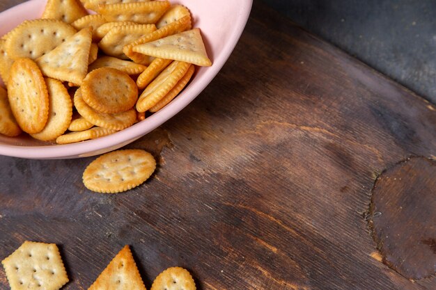 Rosafarbene Platte der Draufsicht mit Crackern und Chips auf dem Knusper-Crackersnackfoto des grauen Hintergrunds