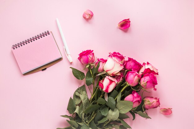 Rosarosenblumen mit Notizbuch auf Tabelle