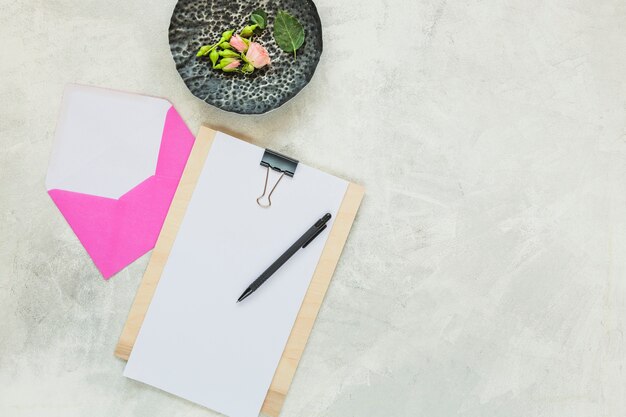 Rose und Knospen auf Steintablett mit rosa Umschlag und Stift in Zwischenablage