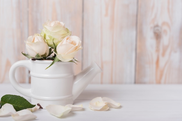 Rosen in der keramischen kleinen Gießkanne auf hölzernem Schreibtisch