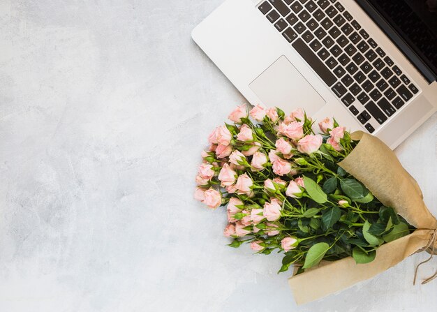 Rosenblumenstrauß mit einem offenen Laptop auf konkretem Hintergrund