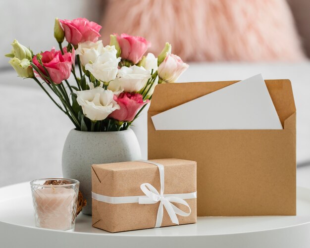Rosenstrauß in einer Vase neben verpacktem Geschenk und Umschlag