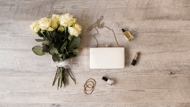 Rosenstrauß; kupplung; parfüm; lippenstift; nagellack und haarbänder auf hölzernen hintergrund