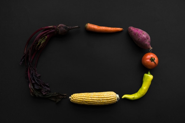 Kostenloses Foto rote beete; karotte; süßkartoffel; tomate; grüner paprikapfeffer und maiskolben, die rahmen auf schwarzem hintergrund bilden