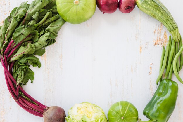 Rote-Bete-Blätter; Kohl; Kürbis; Zwiebel; Zucchini; grüne Bohnen und grüner Pfeffer auf weißem hölzernem Schreibtisch