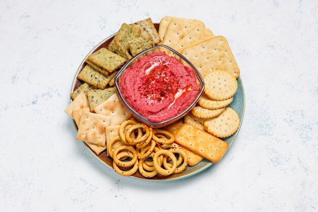 Rote-Bete-Wurzeln Hummus auf Schneidebrett mit salzigen Plätzchen auf heller Oberfläche