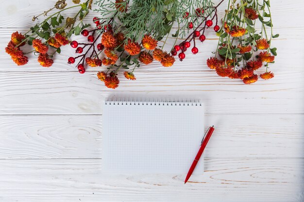 Rote Blumen mit leerem Notizbuch und Stift auf Tabelle