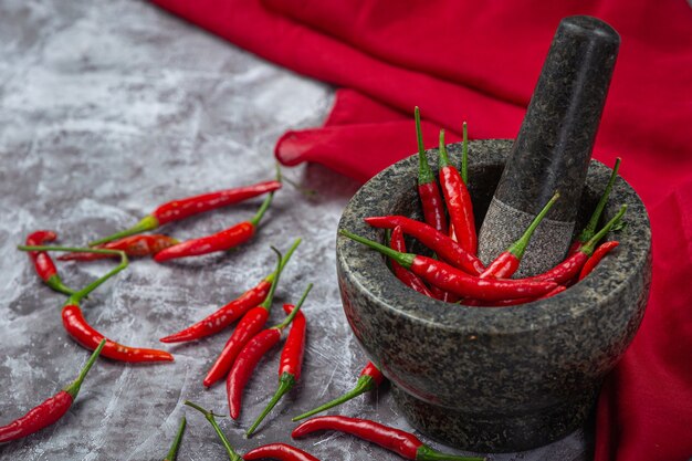 Rote Chilischoten befinden sich in einem Steinmörser auf schwarzer Oberfläche.