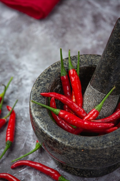 Rote Chilischoten befinden sich in einem Steinmörser auf schwarzer Oberfläche.