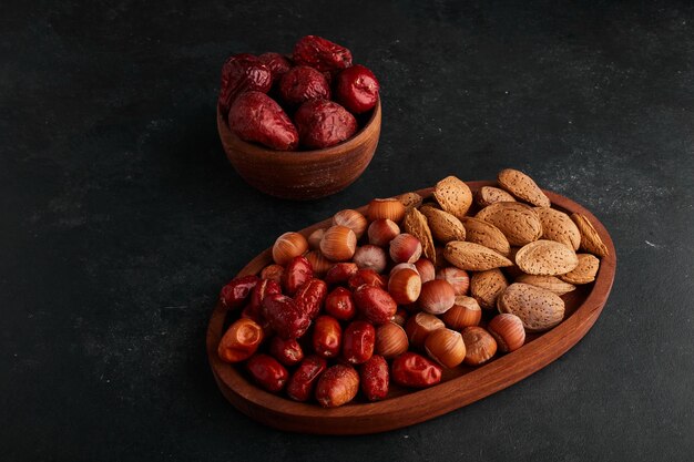 Rote Datteln und Nüsse in einer Holzschale auf Schwarzraum.