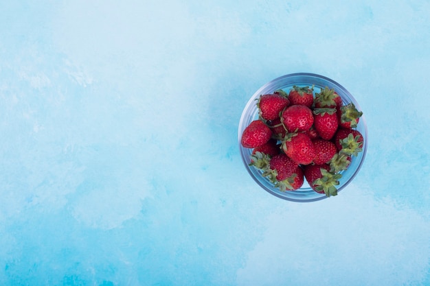 Rote Erdbeeren in einer Glasschale auf Blau rechts.
