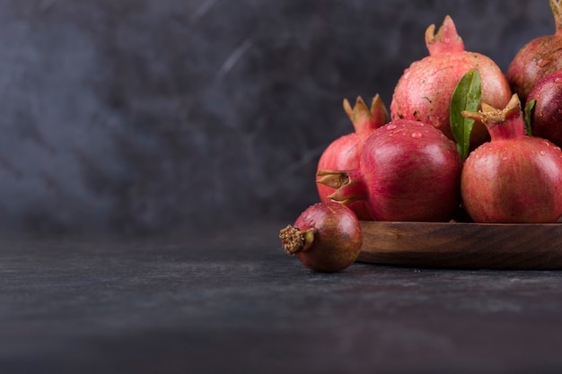 Rote Granatäpfel in einer Holzplatte auf Marmor