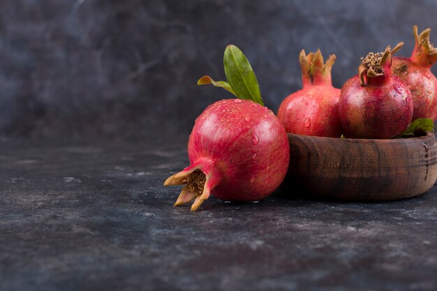 Rote Granatäpfel in einer Holzplatte und auf dem Marmortisch