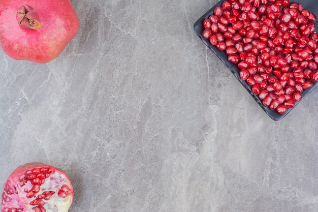 Rote Granatäpfel und Teller der Samen auf Steinhintergrund.