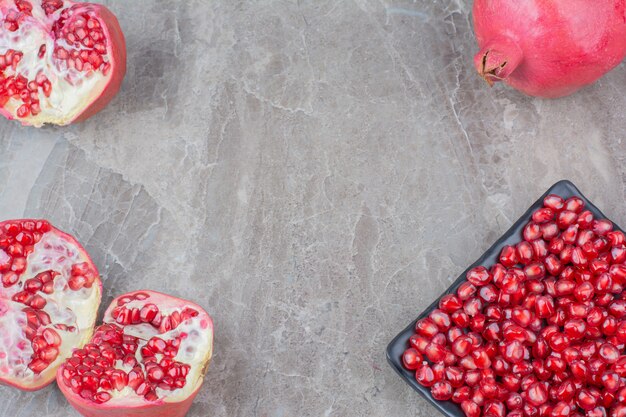 Rote Granatäpfel und Teller der Samen auf Steinhintergrund.