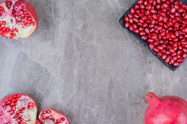 Rote Granatäpfel und Teller der Samen auf Steinhintergrund.