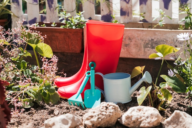 Rote Gummistiefel; Gießkanne und Gartengeräte im Garten