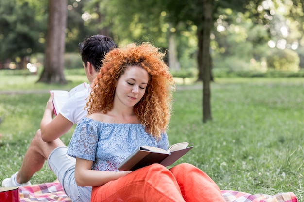 Rote Haarfrau, die auf einer Picknickdecke liegt und ein Buch liest