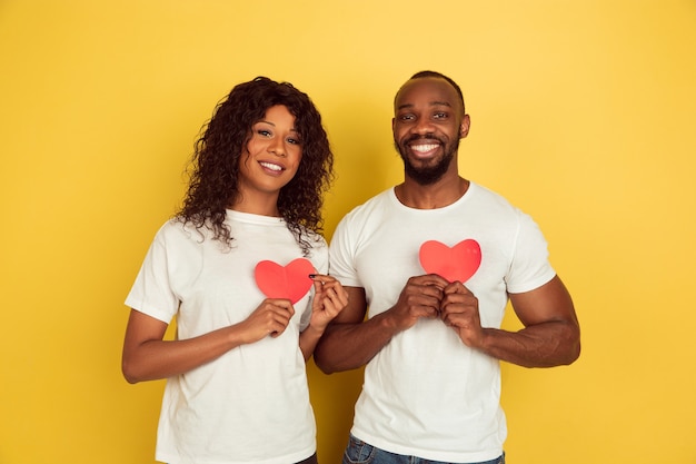 Rote Herzen halten. Valentinstagfeier, glückliches Afroamerikanerpaar lokalisiert auf gelbem Studiohintergrund. Konzept der menschlichen Gefühle, Gesichtsausdruck, Liebe, Beziehungen, romantische Feiertage.