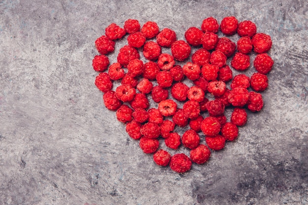 Rote Himbeeren in einer Herzform auf einem grauen Tisch. Draufsicht.