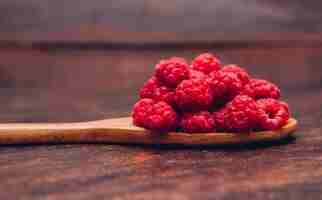 Kostenloses Foto rote himbeeren in einer holzlöffel-seitenansicht auf einem holztisch