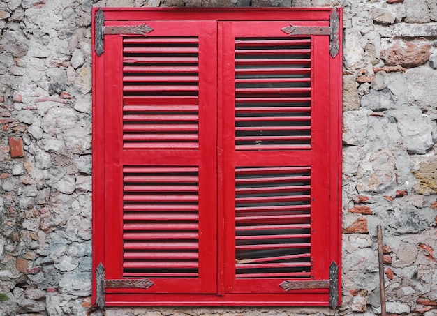 Rote Holzjalousien schließen das Fenster an der alten Steinmauer des Hauses Alte Ziegelwandidee für Innen- oder Loftstudio und Innenhof