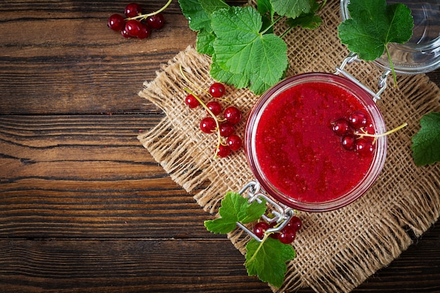 Rote Johannisbeermarmelade in einem Glas auf einer Holzoberfläche. Leckeres Essen.