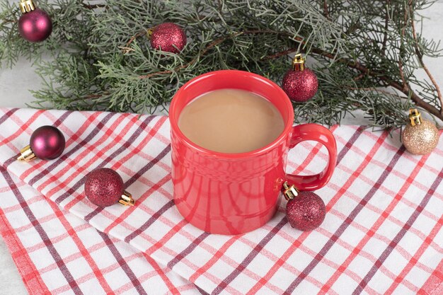 Rote Kaffeetasse auf Tischdecke mit Weihnachtskugeln und Tannenzweig