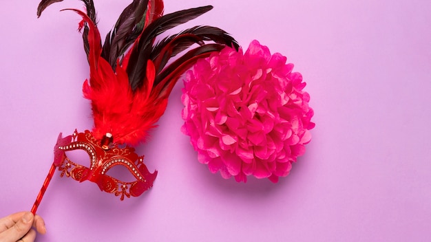 Rote Karnevalsmaske mit Federn auf rosa Hintergrund