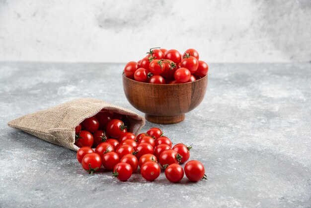 Rote Kirschtomaten aus einem rustikalen Korb und in einer Holzschale auf Marmortisch.