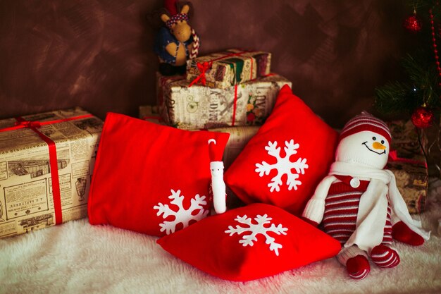 Rote Kissen mit Schneeflocken und Spielzeugschneemann liegen auf dem Boden